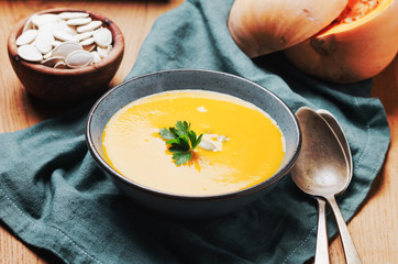 Pumpkin soup in blue bowl with pasrley and seeds.