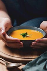 Female hand holding a  bowl with pumpkin cream soup. Cozy comfort concept.
