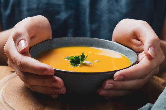 Female hand holding a  bowl with pumpkin cream soup. Cozy comfort concept.