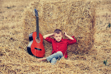 Naklejka na ściany i meble Portrait of a romantic boy in the field .A boy in a haystack with an acoustic guitar