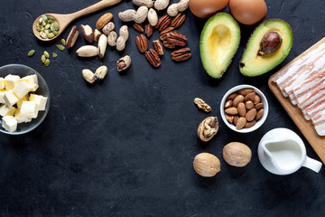 Keto diet food: avocado, nuts, eggs, seeds, cream on black background, top view