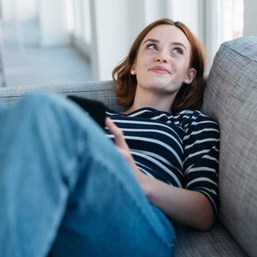 Happy young woman lying daydreaming on a sofa