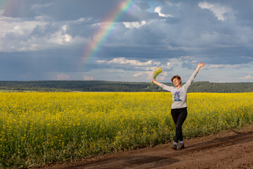 Fototapeta premium A girl is walking along a rural road through a blooming yellow field. Sunny summer day