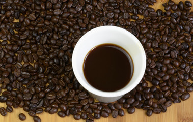 White cup of coffee on table with coffee beans.
