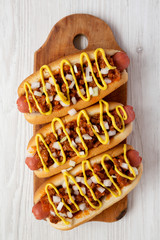 Homemade Coney Island Chili Dog with onion and mustard on a rustic wooden board on a white wooden...