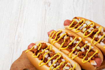 Homemade detroit style chili dog on a rustic wooden board on a white wooden background, low angle...