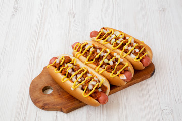 Homemade detroit style chili dog on a rustic wooden board on a white wooden background, low angle view. Close-up.