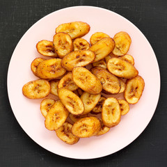 Homemade fried plantains on a pink plate on a black surface, top view. Flat lay, from above, overhead.