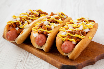 Homemade Coney Island hot dog on a rustic wooden board on a white wooden surface, side view....