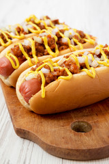 Homemade Detroit style chili dog on a rustic wooden board on a white wooden surface, side view. Closeup.