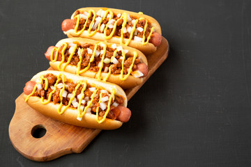Homemade Detroit style chili dog on a rustic wooden board on a black surface, side view. Copy space.