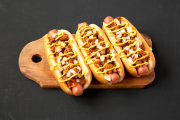 Homemade Detroit style chili dog on a rustic wooden board on a black background, side view....