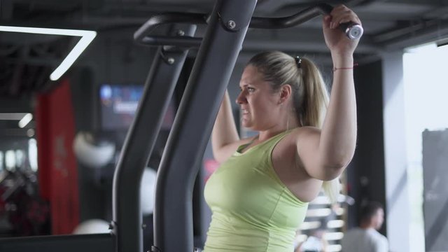 Plus Size Model, woman trains in Gym, performs pull-ups on the simulator, gym equipment.