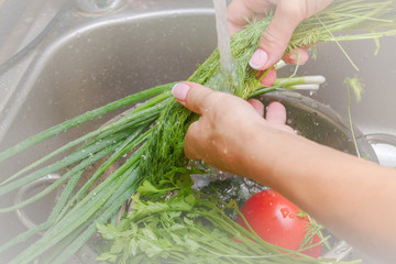 Tomatoes, cucumbers and greens washes with water under the tap young woman
