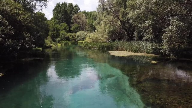 Beautiful slow drone flight above a crystal clear Tirino river in the Abruzzo region in Italy. Lush vegetation, Dragonflies and Mountains.
