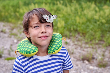 A child in a striped T-shirt with a big butterfly on his head against the background of grass
