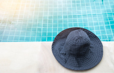 Fototapeta na wymiar Women design summer fabric hat on swimming pool edge over blurred blue water background, design blue fabric hat, outdoor vintage warm light