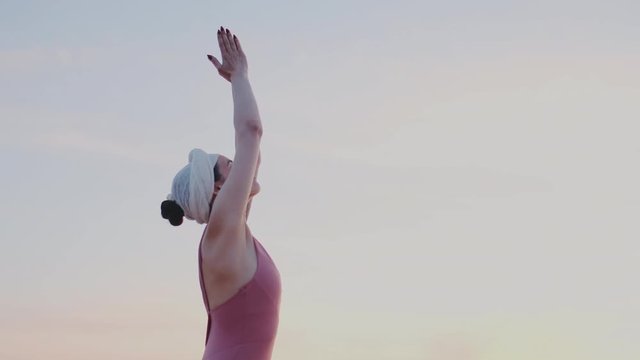 Cute girl raises her hands up to the sky, does namaste. Greetings to the sun, the traditional asana of Indian yoga. Sun beams into the camera. recreation, spiritual, wellness, workout.