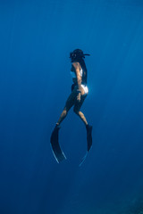 Young woman in a sexy swimwear ascends to the surface after a deep dive.