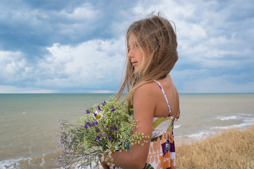 Portrait of a girl with a bouquet of wild flowers on the background of the sea and blue sky