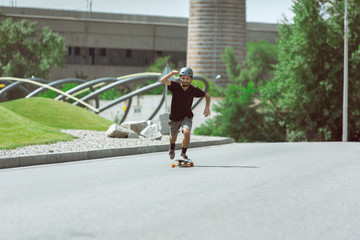 Skateboarder doing a trick at the city's street in sunny day. Young man in equipment riding and longboarding on the asphalt in action. Concept of leisure activity, sport, extreme, hobby and motion.