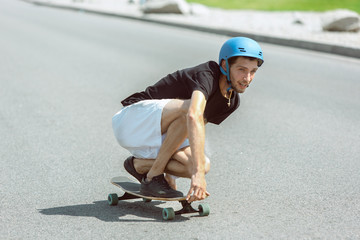 Skateboarder doing a trick at the city's street in sunny day. Young man in equipment riding and longboarding on the asphalt in action. Concept of leisure activity, sport, extreme, hobby and motion.