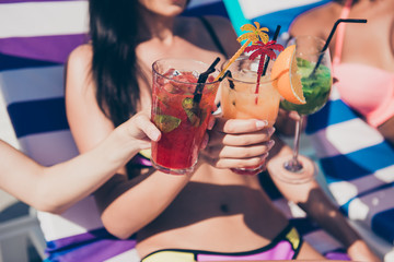 Close-up cropped view of nice attractive slim fit girls sitting on sunbed at fashionable spa resort hotel club having fun clinking glasses congrats greetings seasonal event gathering