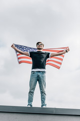 handsome man in glasses holding american flag and smiling on roof