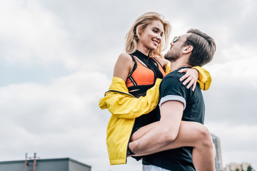 handsome man in glasses holding attractive woman in yellow jacket on roof