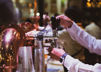 Bartender pouring draft beer in the bar, Barman hand at beer tap pouring draught lager beer serving in a restaurant or pub