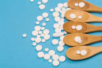Assorted pharmaceutical medicine pills, tablets and capsules on wooden spoon. blue background