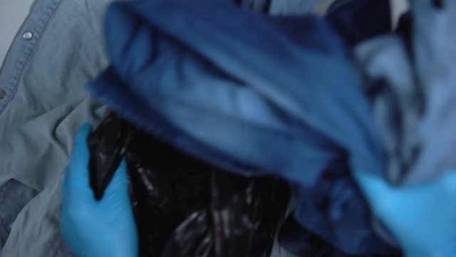 Hands in protective gloves packing used denim clothing in plastic bag, dispose