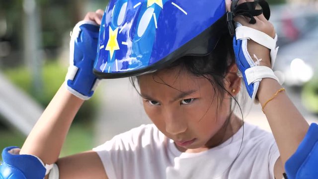 Happy Asian girl wearing helmet and headguard for playing roller blades in the park outdoor.