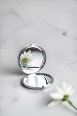 White flower is reflected in the mirror on light marble background. Beauty concept