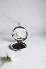 White flower is reflected in the mirror on light marble background. Beauty concept