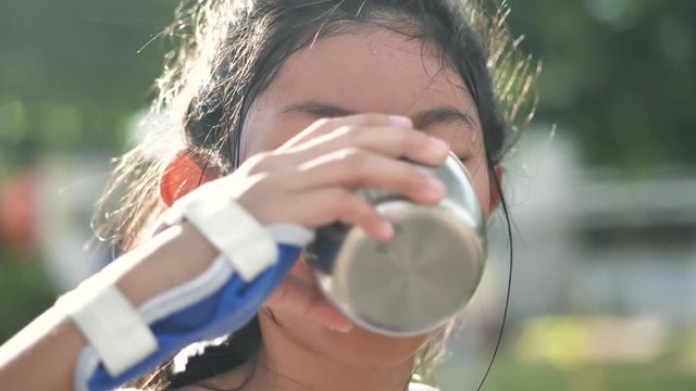 Asian girl pouring water from thermos bottle and drinks in the park outdoor, lifestyle concept.