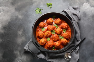 Meatballs in sweet and sour tomato sauce with spices served in a frying pan on dark background . Top view