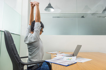 Tired Asian employee stretching in front of computer at office