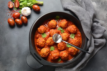 Meatballs in sweet and sour tomato sauce with spices served in a frying pan on dark background . Top view