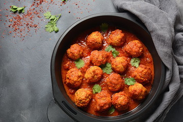 Meatballs in sweet and sour tomato sauce with spices served in a frying pan on dark background . Top view 