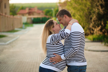 Happy pregnant woman and her husband kissing and hugging, posing on the street.