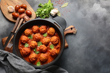Meatballs in sweet and sour tomato sauce with spices served in a frying pan on dark background . Top view 