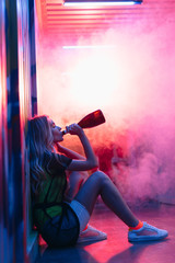 side view of attractive and blonde woman sitting on floor and drinking champagne
