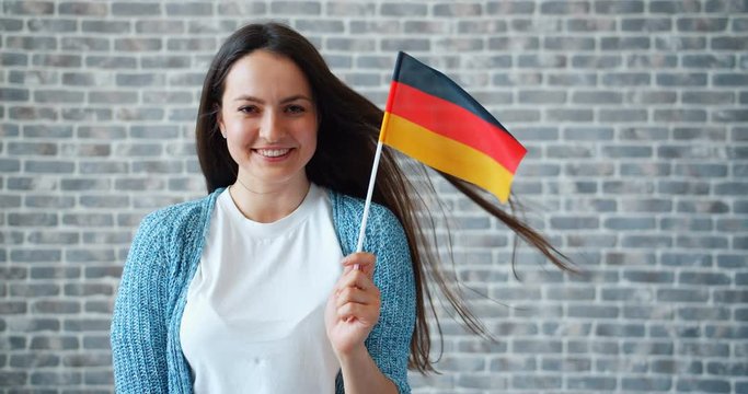 Portrait of attractive young woman holding national German flag standing on brick wall background and smiling. Patriotism, youth and world tourism concept.