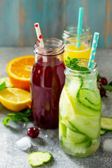 Various refreshments drinks - detox cucumber water, cherry juice and orange juice on stone table.