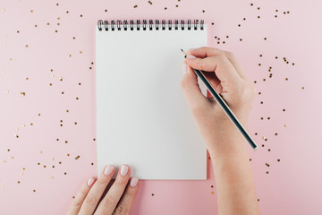 Woman's hand writing in empty notebook decorated with Christmas decorations on the blue background....