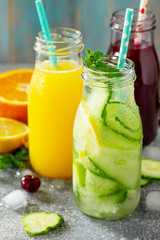 Various refreshments drinks - detox cucumber water, cherry juice and orange juice on stone table.