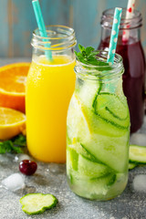 Various refreshments drinks - detox cucumber water, cherry juice and orange juice on stone table.
