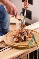 Man holds a round wooden board with pieces of fried meat and green onions