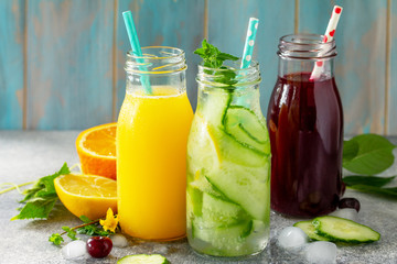 Various refreshments drinks - detox cucumber water, cherry juice and orange juice on stone table.